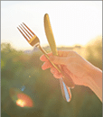 Steel metal shiny knife and fork in a womans hand, background sunset, evening city